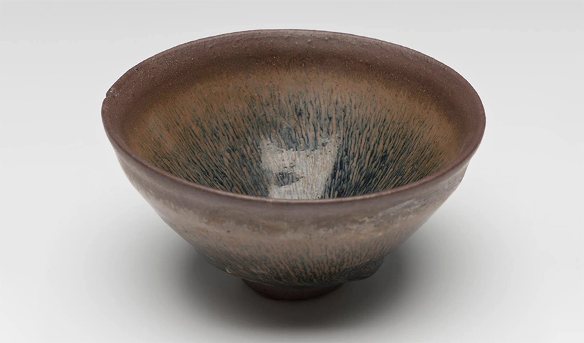 photo of a dark glazed ceramic bowl against a light gray background shot from slightly above
